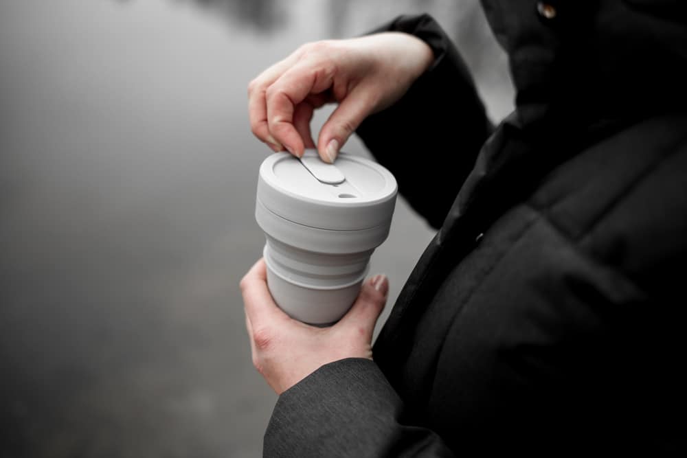 A man opens the lid of a reusable mug.