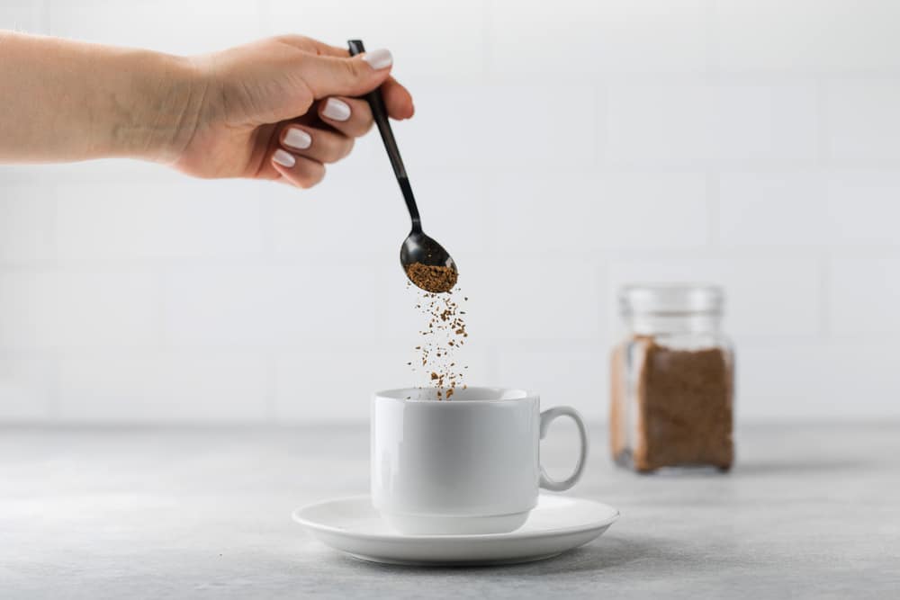 A woman adds decaffeneited granules to a white mug